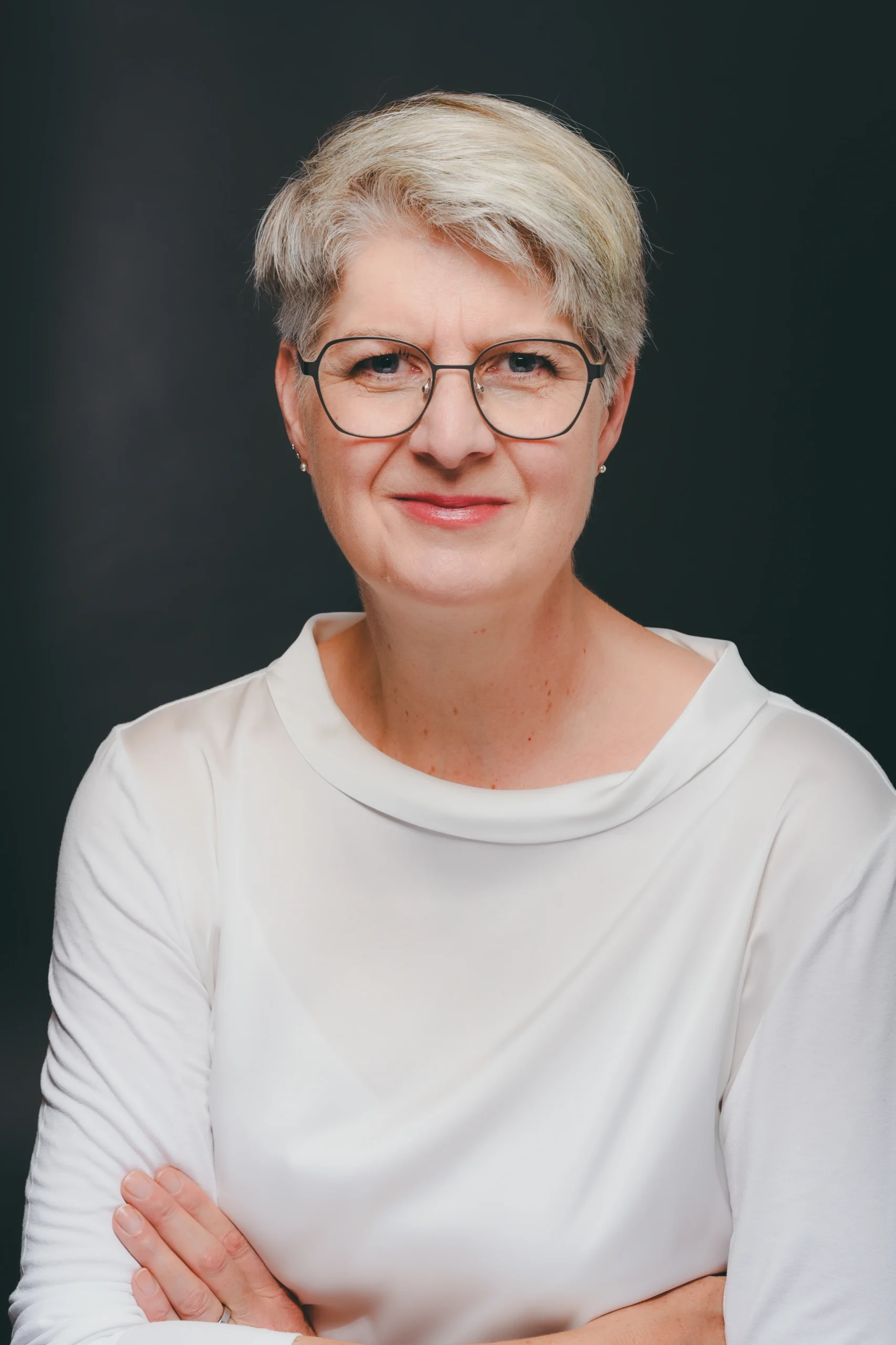 Anne Komp, Porträtfoto vor dunklem Hintergrund, verschränkte Arme.